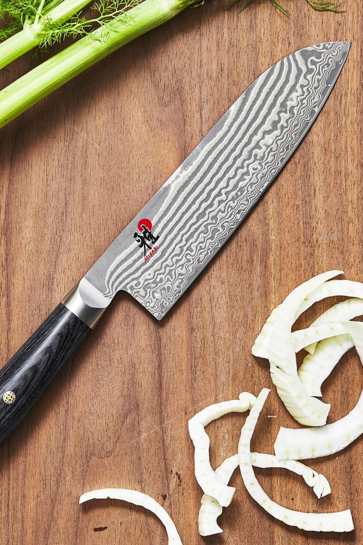 Et nærbilde av den japanske Santoku-kniven fra Miyabi på en skjærefjøl av tre med oppkuttede grønnsaker.