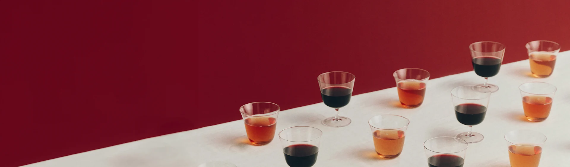 Ulike glass med røde og ravfargede drikker på en hvit overflate med rød bakgrunn.